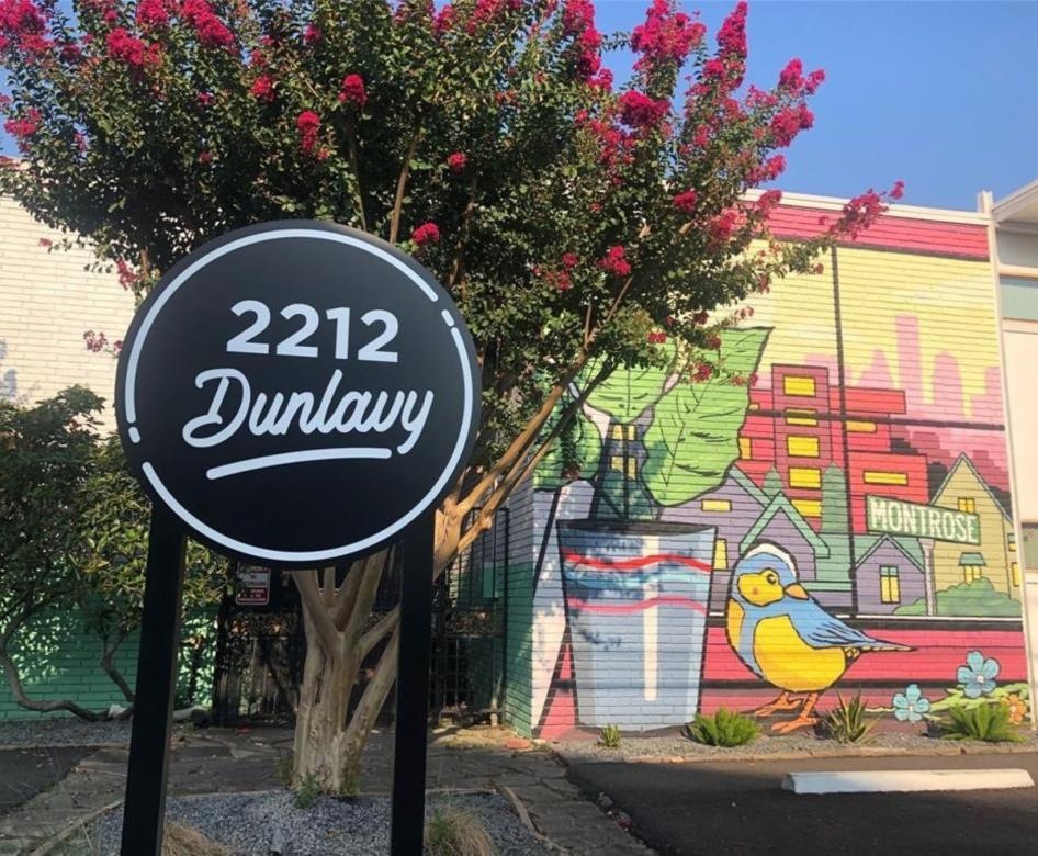a sign with a tree and building behind it